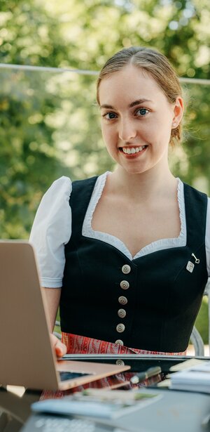 Junge Dame in Tracht sitzt vor einem Laptop und schaut nach einem Job in Schmallenberg im Sauerland.