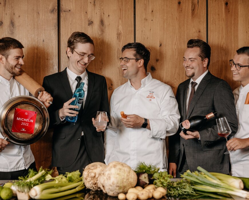 Eine Gruppe mehrere Männer probiert Wein und zeigt eine Pfanne mit der Auszeichnung Michelin 2022.