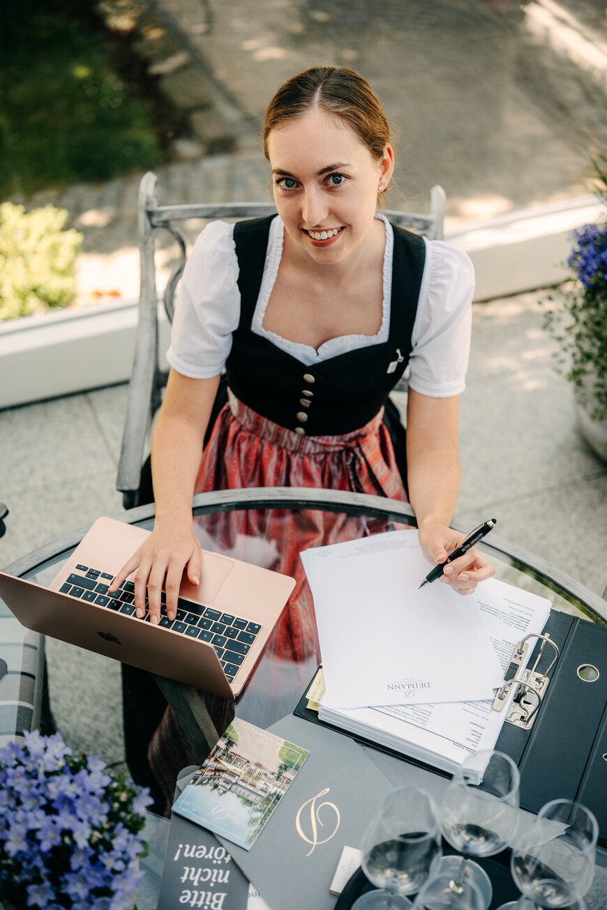 Junge Frau in Tracht sitzt vor ihrem Laptop und macht Notizen während ihrer Ausbildung in Schmallenberg.