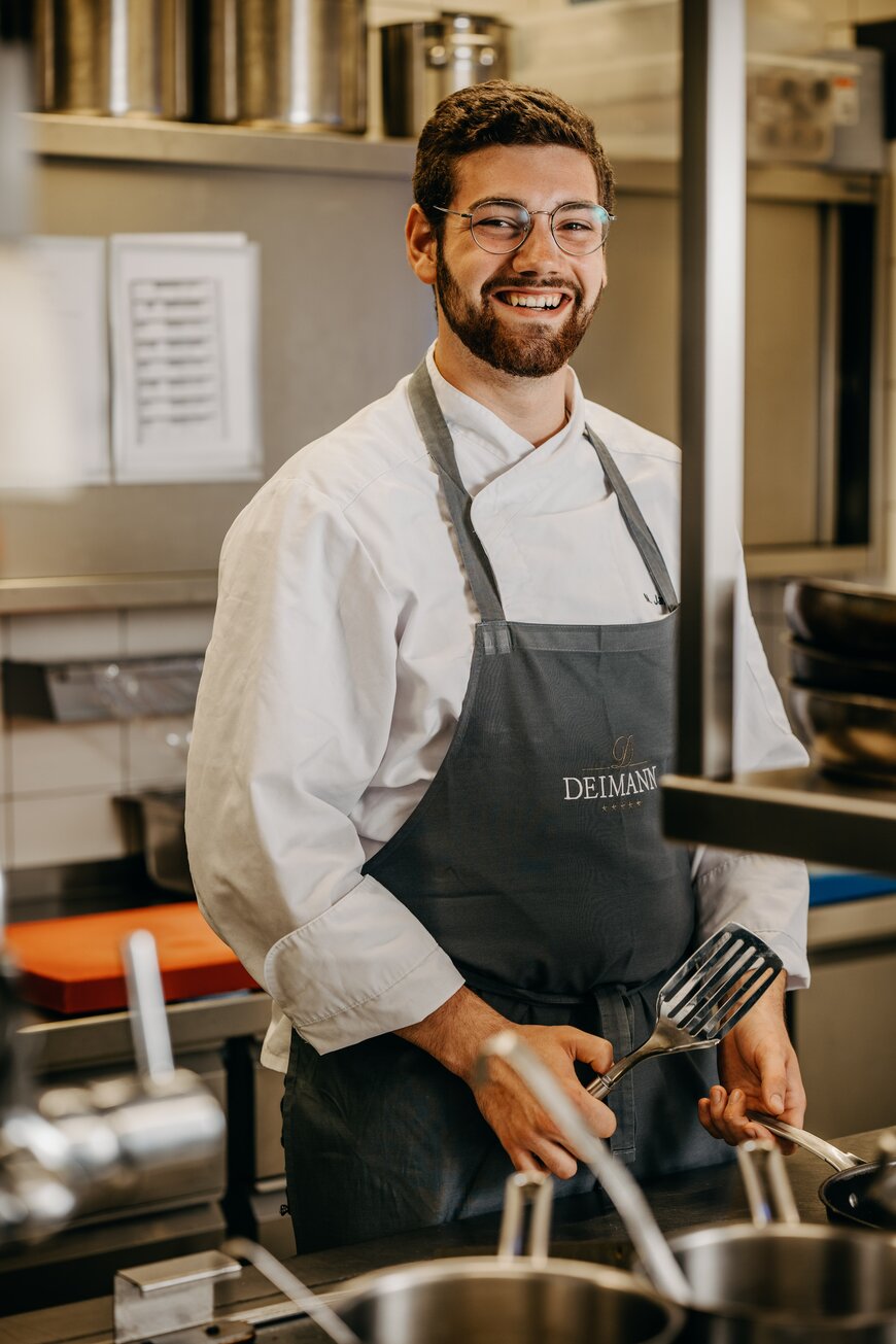 Lächelnder Koch in der Hotelküche während seiner Ausbildung in Schmallenberg im Sauerland.