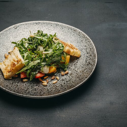 Detailaufnahme eines Salates mit Fisch garniert angerichtet auf einem grauen Teller.
