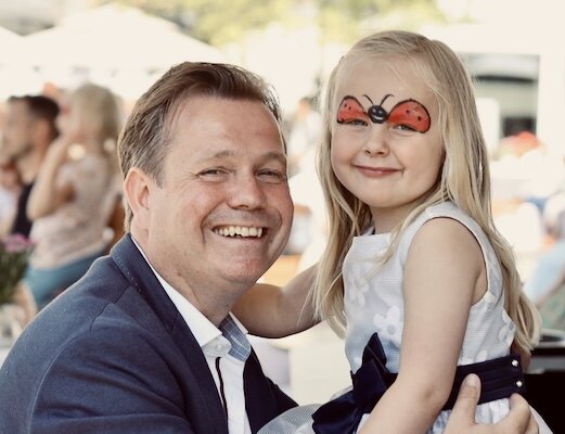 Ein Vater hält seine Tochter im Arm. Das Mädchen hat eine Schmetterling-Gesichtsbemalung.
