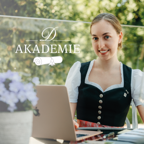 Eine Frau in Tracht sitzt vor Ihrem Laptop und neben Ihr erscheint ein Symbol "Akademie".