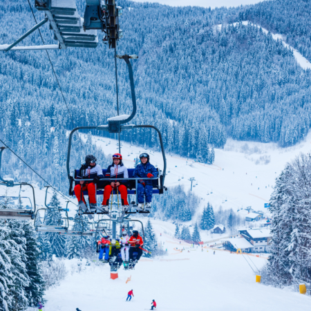 Eine Gruppe von drei Personen sitzt auf einem Ski-Lift und fährt einen verschneiten Berg hinauf.